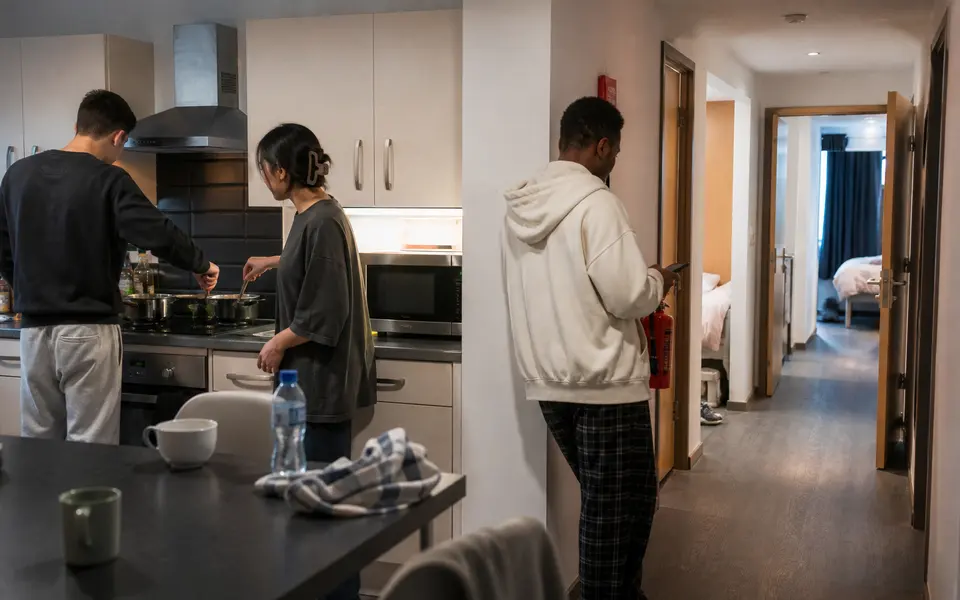 Students cooking together in a shared Manchester student flat kitchen with individual bedrooms off a corridor.