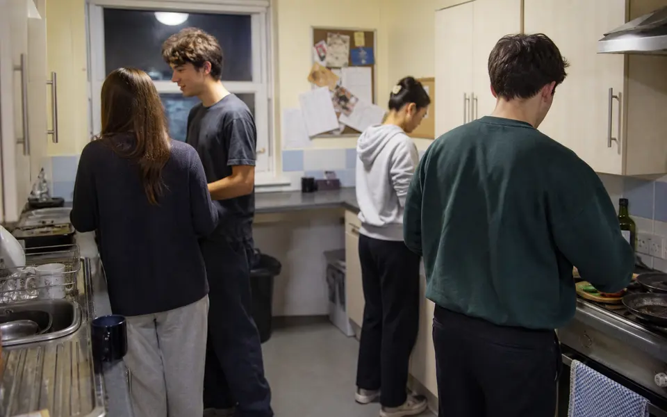 Students cooking together in a small shared kitchen in a London student flat.