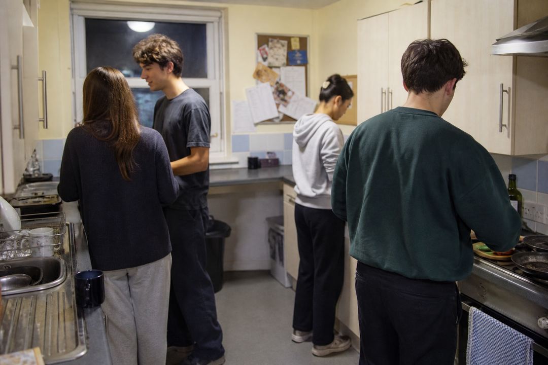Students cooking together in a small shared kitchen in a London student flat.