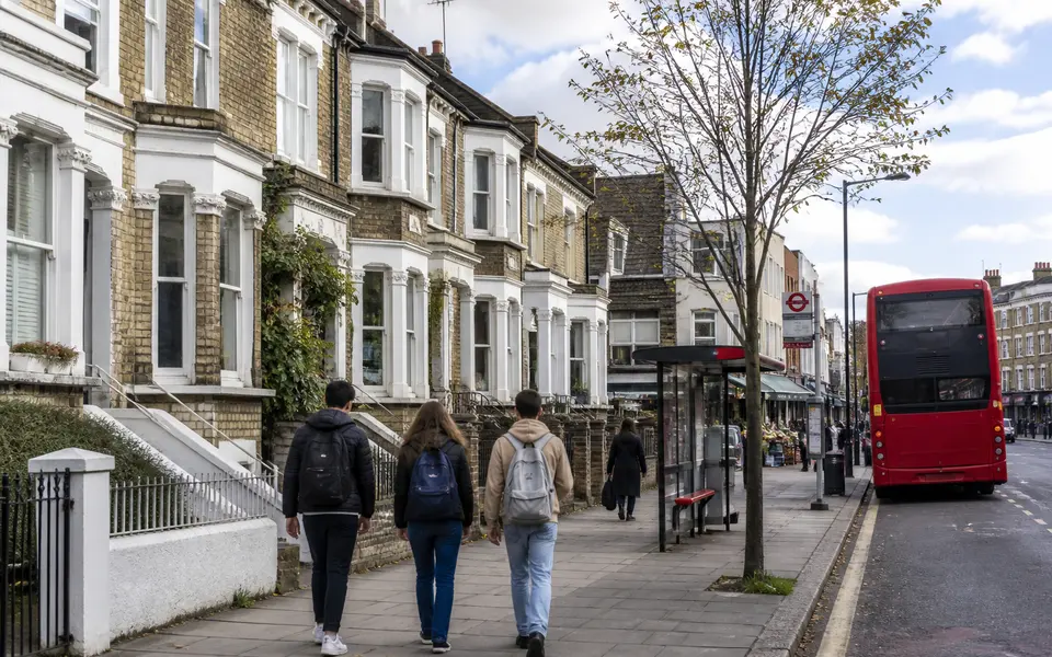 Street view of a typical London student neighbourhood with terraced housing, a bus stop and students walking.