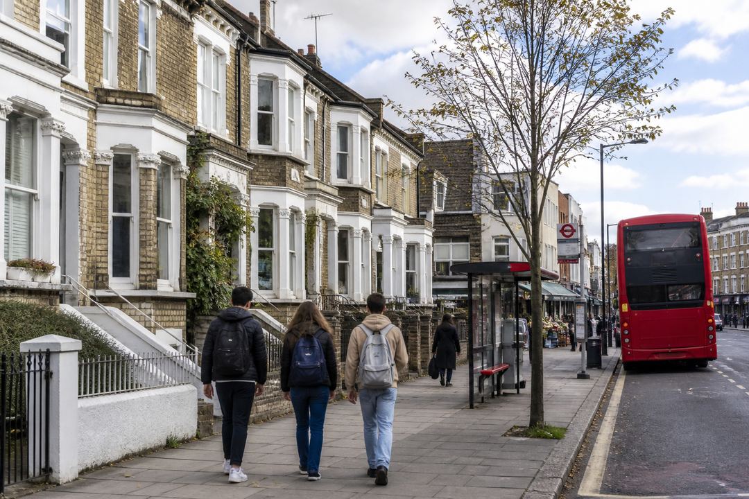 Street view of a typical London student neighbourhood with terraced housing, a bus stop and students walking.